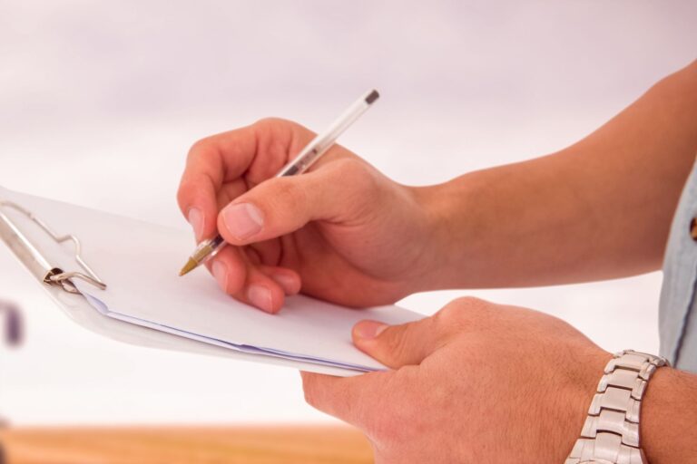 A man's hand with pen on a plain paper to be used as a checklist.