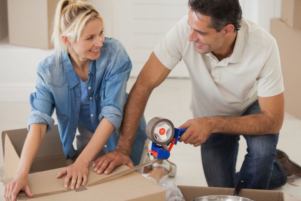 A couple is smiling while packing a box; in the concept of packing efficiently for a house move.