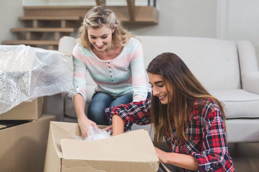 Friends are happy unpacking their carton boxes after moving in.