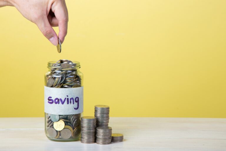 A hand is putting a coin into a jar in the concept of saving money for moving to Canary Wharf.