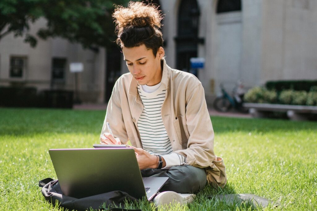 A student is on the lawn with his laptop